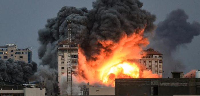 Un grupo de personas en una azotea observa cómo una bola de fuego y humo se eleva sobre un edificio en la ciudad de Gaza el 7 de octubre de 2023 durante un ataque aéreo israelí.Mahmud Hams/AFP.